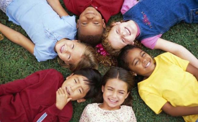 diverse children laying on the grass in a circle looking up at the sky